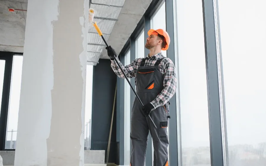 Commercial painter in a hard hat rolling paint onto an office wall with an extension pole, West Palm Beach, FL