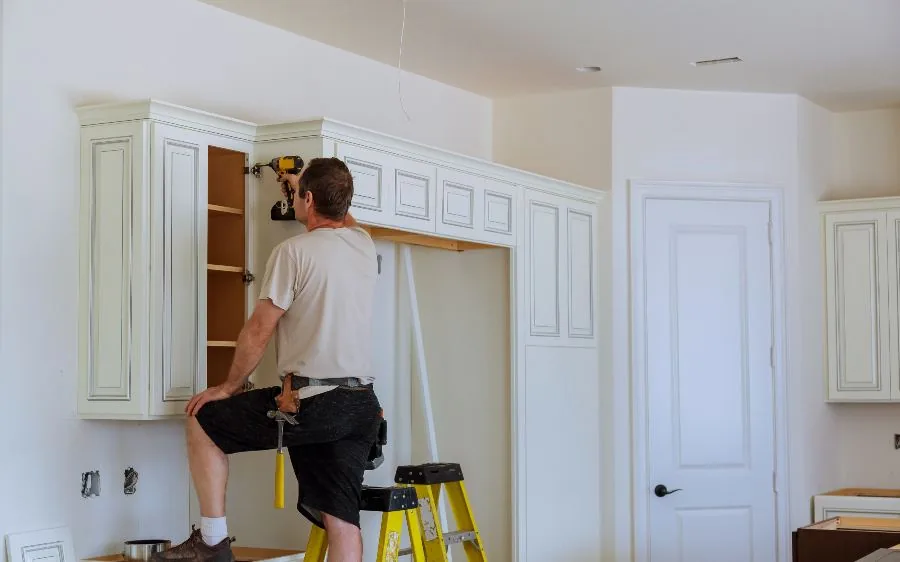 Painter on a ladder rehanging freshly painted white kitchen cabinet doors, Palm Beach Gardens, FL