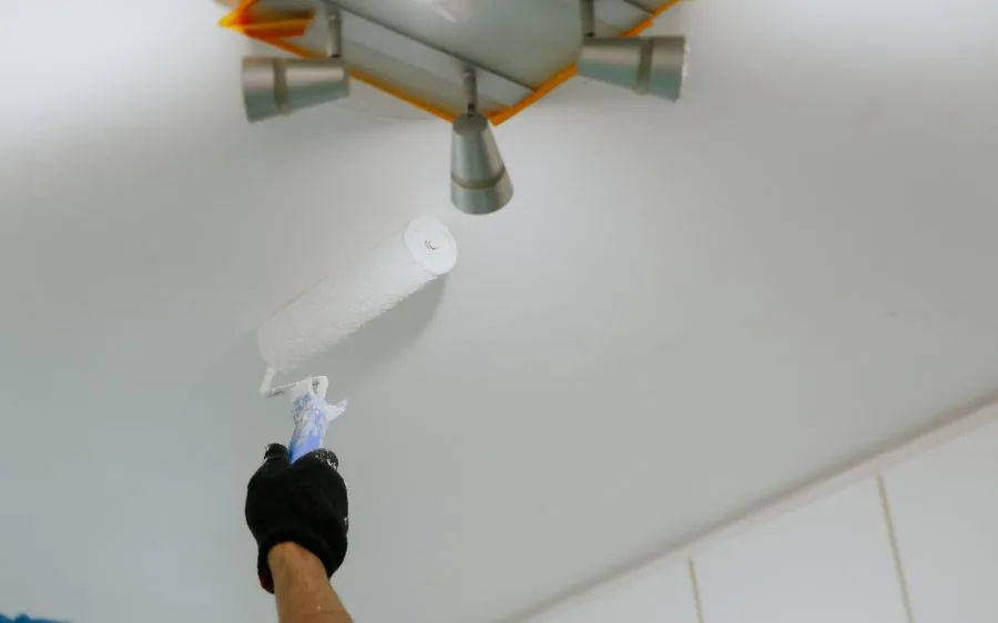 Painter rolling fresh white paint onto a smooth ceiling around a masked light fixture, West Palm Beach, FL