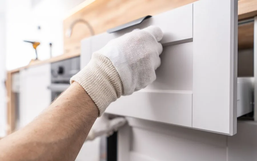 Close-up of a painter's gloved hand checking a smooth white painted cabinet drawer front, Boca Raton, FL